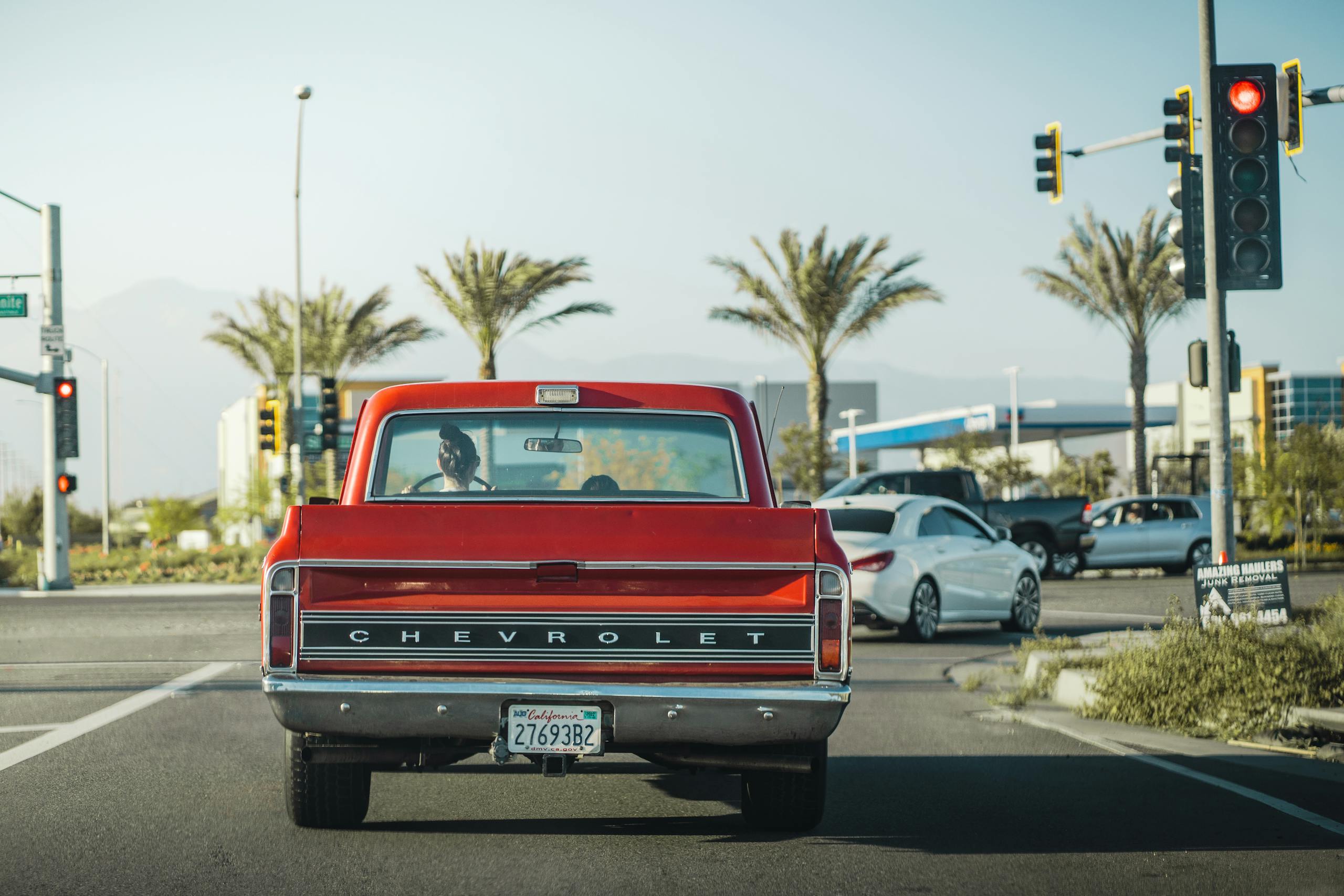 Red vintage Chevrolet truck at traffic light in Los Angeles street backdrop with palm trees.